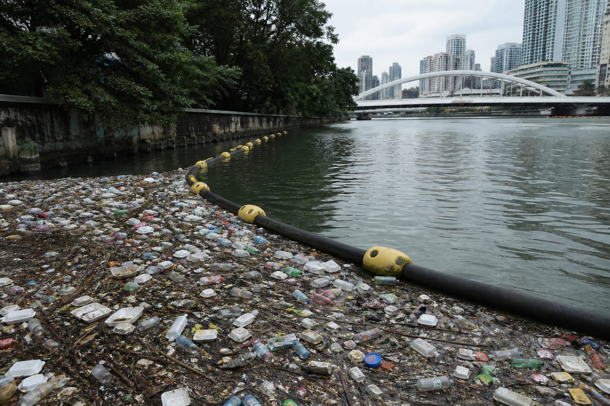 Floating river boom with yellow buoys holding back plastic bottles and litter